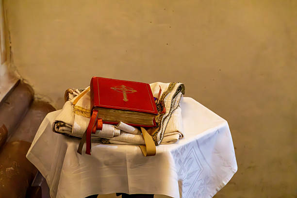small round table covered with a white tablecloth, on which a red liturgical missal with a cross on the cover and several liturgical vestments were placed. The scene was captured inside the church