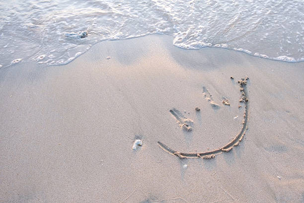 istock A smiley face drawing on a sand at the beach 2211125043