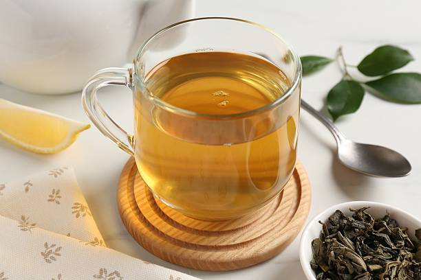 istock Refreshing green tea in cup and leaves on white table, closeup 2211125260