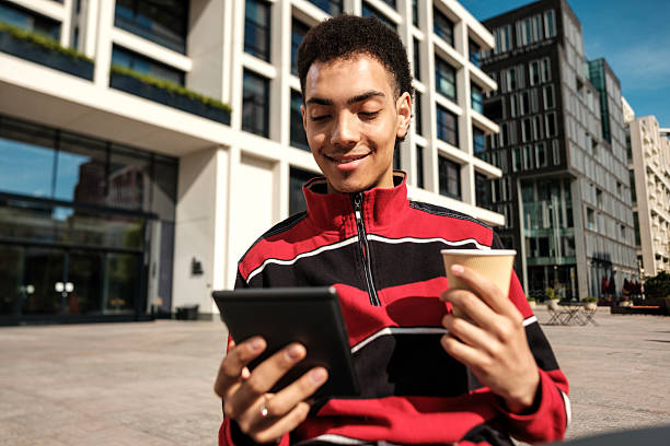 istock Young man using tablet and drinking coffee outdoors in the city 2211138656