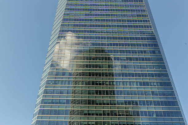 Madrid. Spain. Glass facade of a modern skyscraper reflecting another building and some clouds in the blue sky, representing the concept of modern sustainable architecture