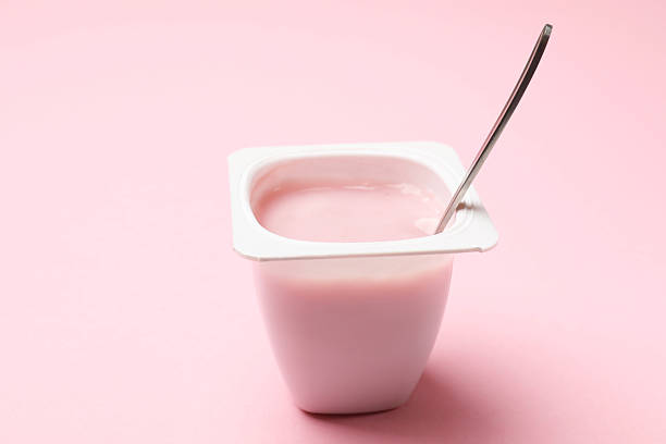 istock Delicious yogurt in plastic cup with spoon on light pink background, closeup 2211144912