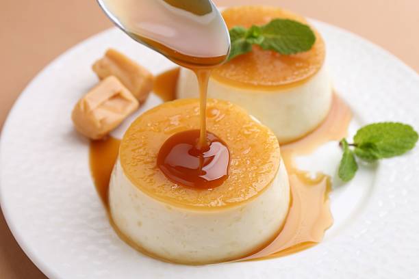 istock Pouring caramel sauce onto tasty pudding on light brown background, closeup 2211149881