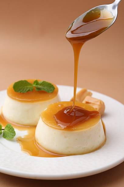 istock Pouring caramel sauce onto tasty pudding on light brown background, closeup 2211149886