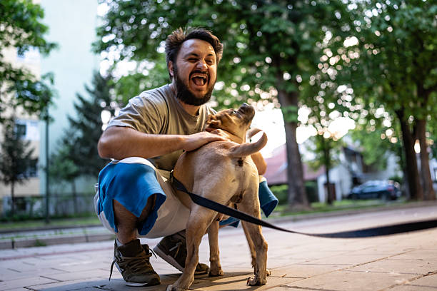 A cheerful man kneeling on a pathway happily spending quality time with his playful dog.