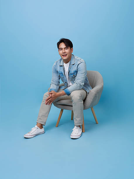 istock Happy young asian handsome man relaxing sitting on sofa isolated on blue background. 2211159848