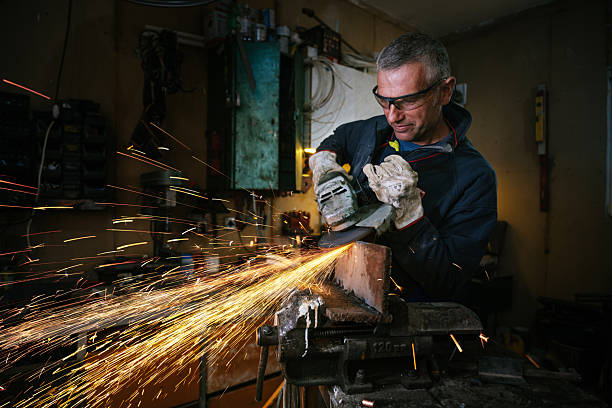 istock Industrial worker in a dimly lit workshop wearing protective goggles and operating an angle grinder with flying sparks around 2211159962