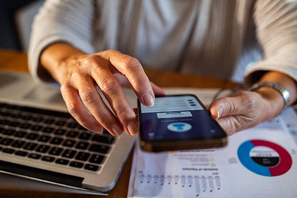 istock Mature woman using a banking app on her smart phone while going over her bills and home finances 2211160538