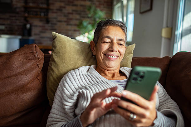 istock Mature woman using a smart phone on a couch at home 2211160646