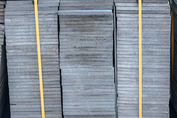 Densely stacked grey slabs of concrete secured with yellow straps. Construction materials in the vicinity