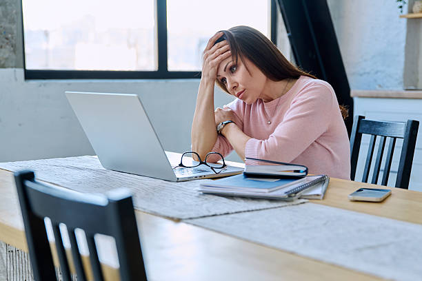 istock Middle aged sad stressed woman sitting at home at table with computer 2211166202