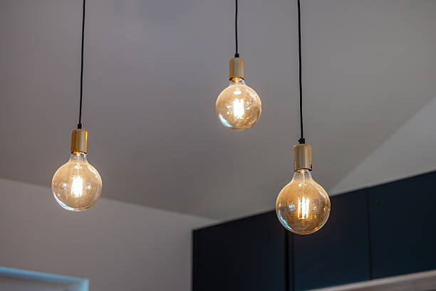 Three exposed Edison bulbs with warm light hang from black cords in a modern room with white walls and dark cabinets, creating a minimalist and industrial ambiance.