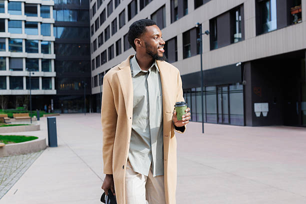 istock Man walking outdoors holding coffee in urban environment on a bright day 2211170347