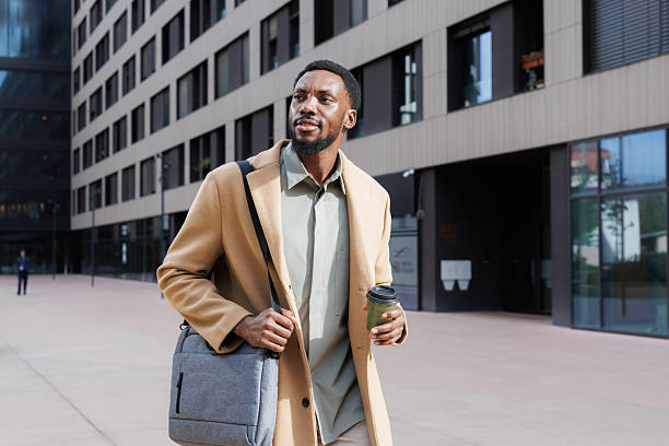 istock Man carrying a laptop bag and coffee walking downtown confidently 2211170348