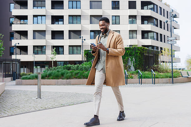 istock Man walking outdoors while using phone near modern residential buildings 2211170371