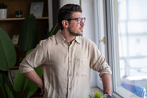 istock Handsome man standing daydreaming through the window. 2211171443