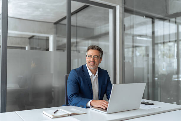 istock Mature Latin business man ceo manager using laptop computer in modern office. Smiling senior businessman entrepreneur sitting at desk working on pc financial project, looking thinking at copy space 2211175035