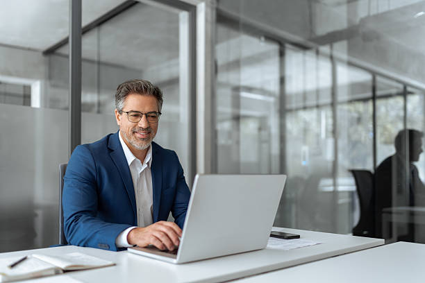 istock Mature Latin business man ceo manager using laptop computer in modern office. Smiling senior businessman entrepreneur sitting at desk working on finance work, looking thinking at screen. Copy space 2211175038