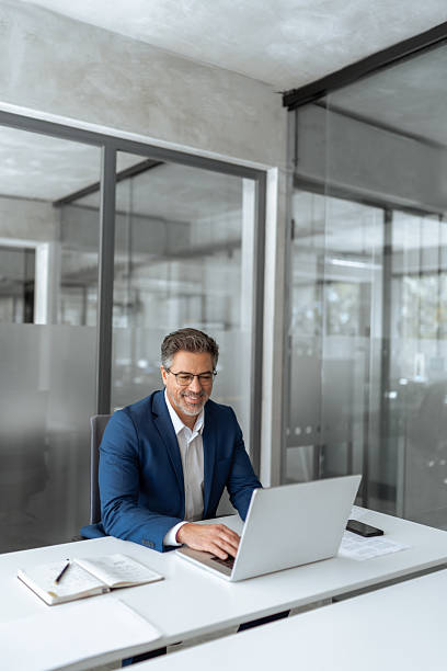 istock Mature Indian or Latin hispanic business man ceo manager using laptop computer typing in modern office. Middle eastern smiling senior businessman entrepreneur sitting at desk working on pc. Vertical 2211175046