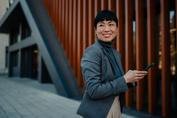 istock Smiling businesswoman using smartphone near office building 2211185672