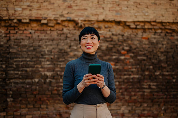 Smiling businesswoman using smartphone in front of brick wall
