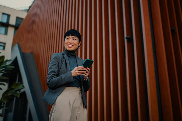 istock Smiling businesswoman using smartphone near modern office building 2211185680