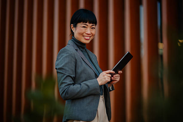 istock Smiling businesswoman using digital tablet outside office building 2211185700