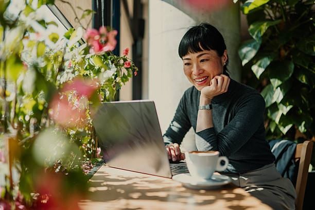 Smiling asian freelancer working on laptop in a sunny cafe
