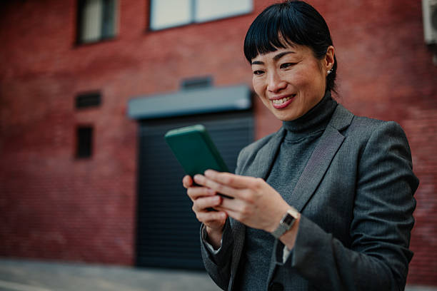 istock Smiling businesswoman using smartphone in front of red brick wall 2211185726