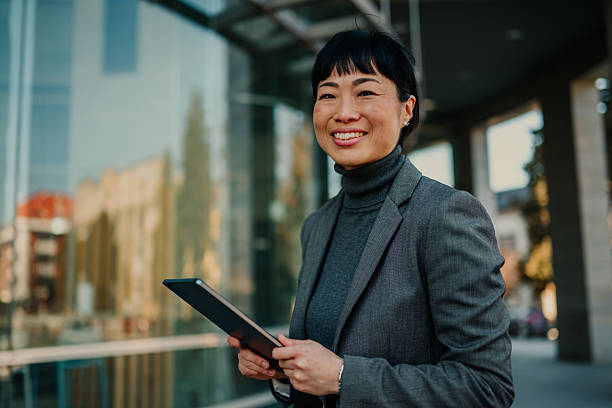 istock Smiling businesswoman using digital tablet in front of office building 2211185730