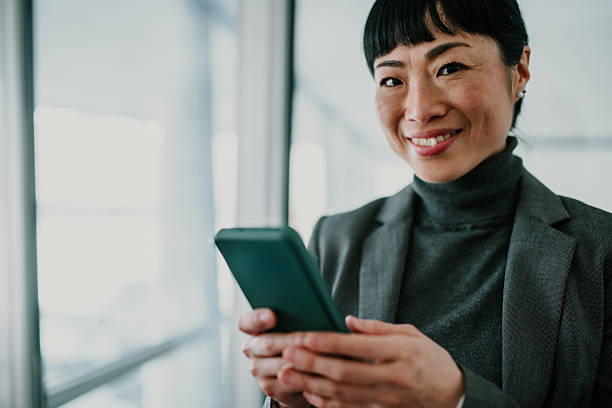 istock Smiling businesswoman using smartphone in office corridor 2211185746