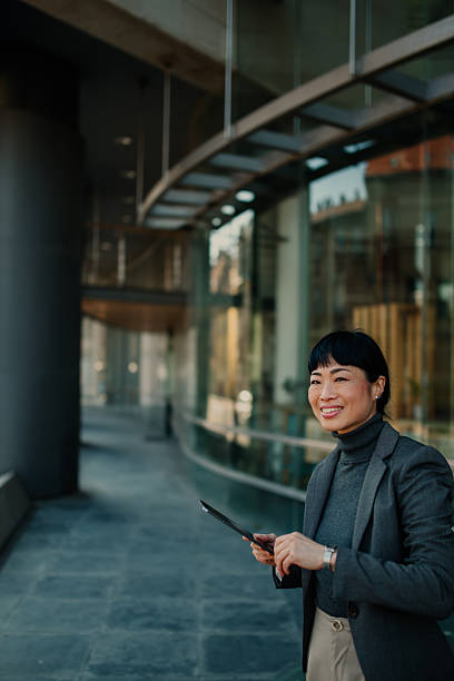 istock Smiling businesswoman using digital tablet outside office building 2211185750