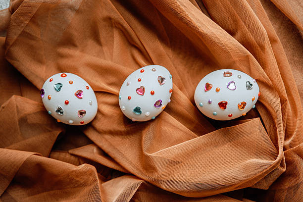 Three uniquely decorated eggs with colorful gems resting on a soft fabric surface.