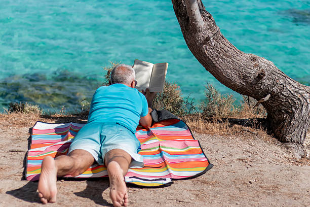 istock Mature man relaxing on the beach, reading a book. 2211188313