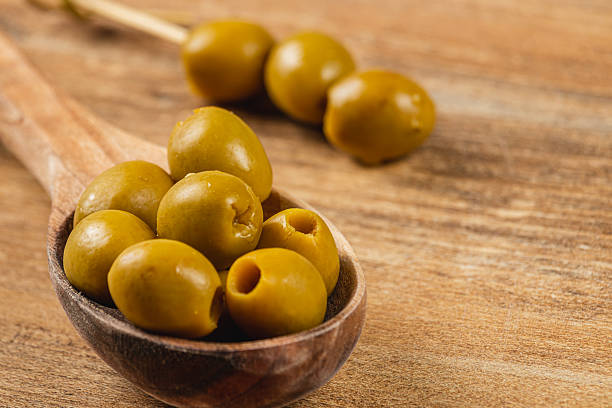 istock Green olives resting on a wooden spoon on a rustic table 2211205673