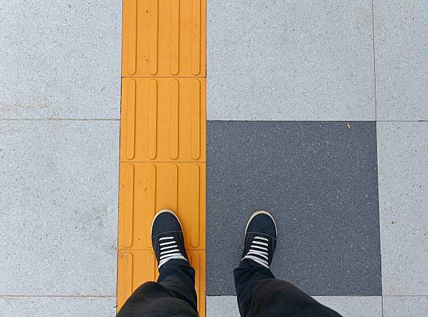 Man standing on the square shaped concrete pavement slabs and tactile paving, top view of black and white shoes with copy space.