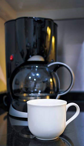 istock Focus on white coffee cup and A modern electronic Drip coffee maker machine with a glass carafe in blurred background, vertical image 2211209533