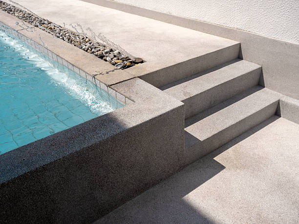 Exposed aggregate finish pool decks with steps with splashing water with no people. Abstract pool texture pattern, light blue background with grid tiles inside concrete building. Summer background.