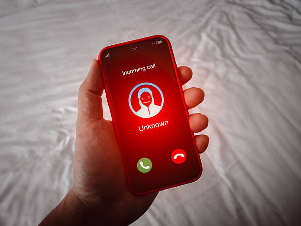 istock Scam call alert with red scammer icon as unknown caller, malicious phone calls concept. Unknown number Incoming displayed showing on smart mobile phone screen in person hand. 2211212003