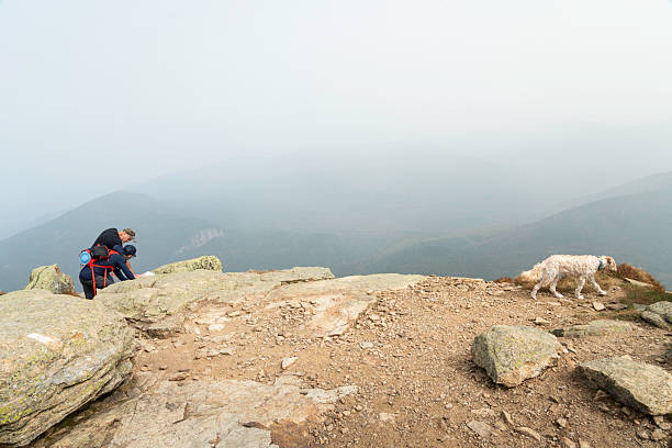 Franconia Notch, New Hamphsire - September 28, 2023: Mature couple analyzes a map while their dag wanders on the  Appalachian Trail on the summit of Mt Lafayette in the White Mountains