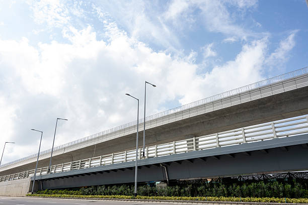 Modern urban infrastructure featuring an elevated roadway with safety barriers, streetlights, and landscaped greenery beneath. The scene is calm and orderly, suitable for transportation or city planning contexts.