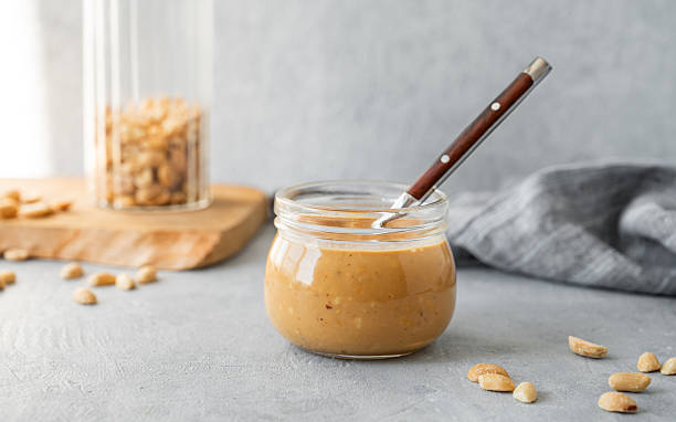 istock Glass jar  with creamy peanut butter on grey background with scattered roasted nuts 2211219138