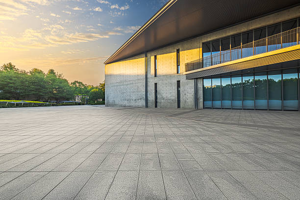 Empty stone paved square floor in front of modern concrete building exterior with large windows during sunrise.