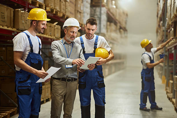 istock Male inspector using touchpad with manual workers in storage room. 2211221001
