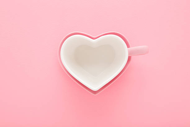 istock Empty heart shape white cup and pink saucer on light pink table background. Pastel color. Closeup. Top down view. 2211222181