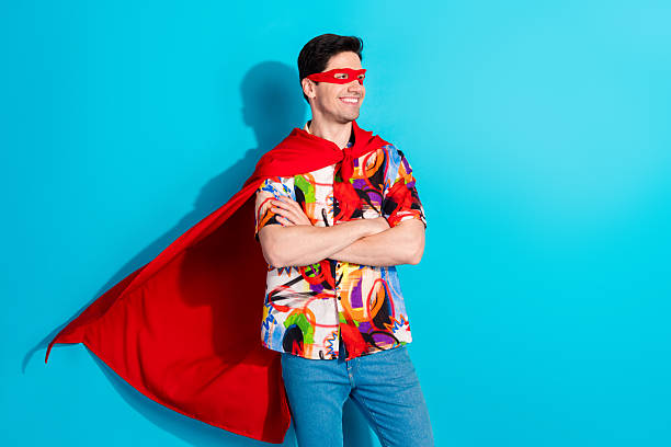 istock Confident young man posing playfully in colorful attire with red cape on blue background showing style and joy 2211222590