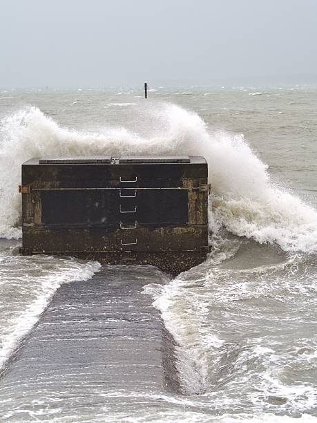 Powerful ocean wave crashing against a pier with overcast skies, showcasing nature's force.