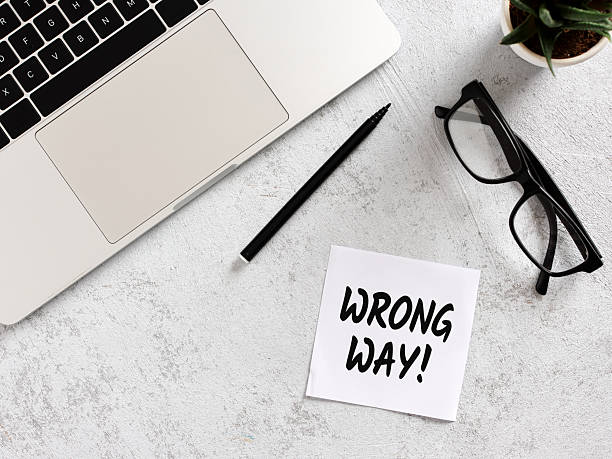 istock Wrong Way message on sticky note with laptop, glasses and pen on desk 2211227952