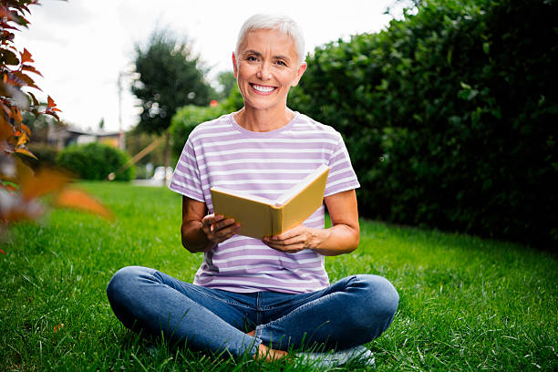 istock Elderly woman enjoying a sunny day outdoors while reading a book in a peaceful park setting, showcasing leisure and happiness 2211230880