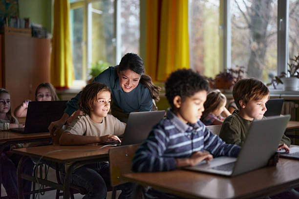 istock Happy female teacher assisting schoolboy with using laptop on a class. 2211231419